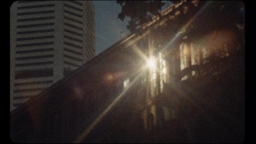 A nostalgic vintage shot captures a sun flare on an old building with a modern skyscraper in the background