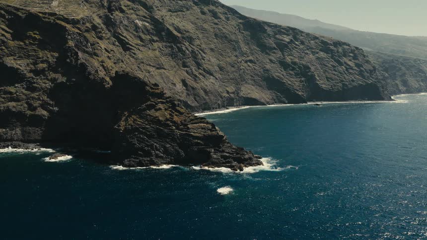 A stunning aerial view shows the majestic cliffs of a volcanic island dropping into the serene blue ocean