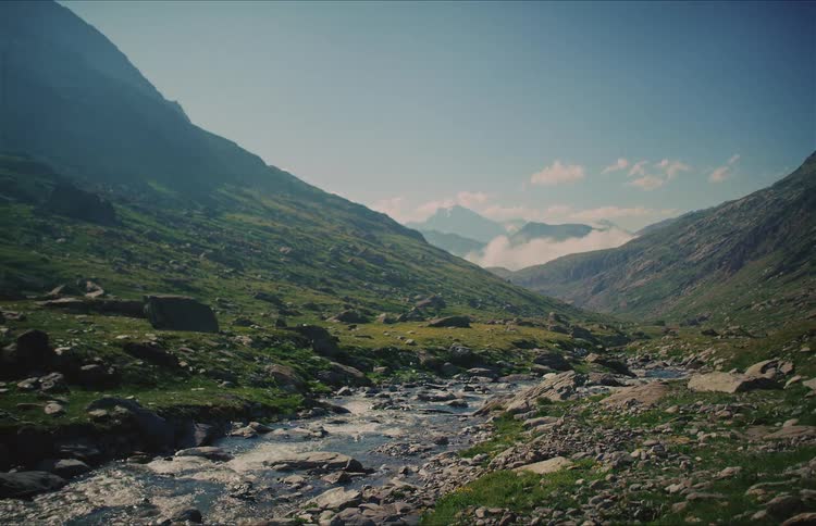 A scenic wide shot of a pristine mountain stream flowing through a lush green valley on a beautiful sunny day