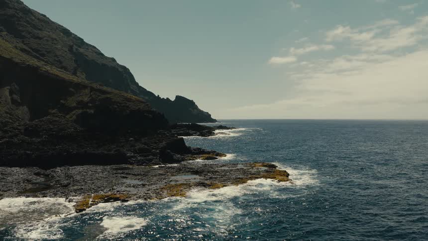 A serene view of the ocean waves gently crashing against a rugged, rocky coastline at the base of a mountain