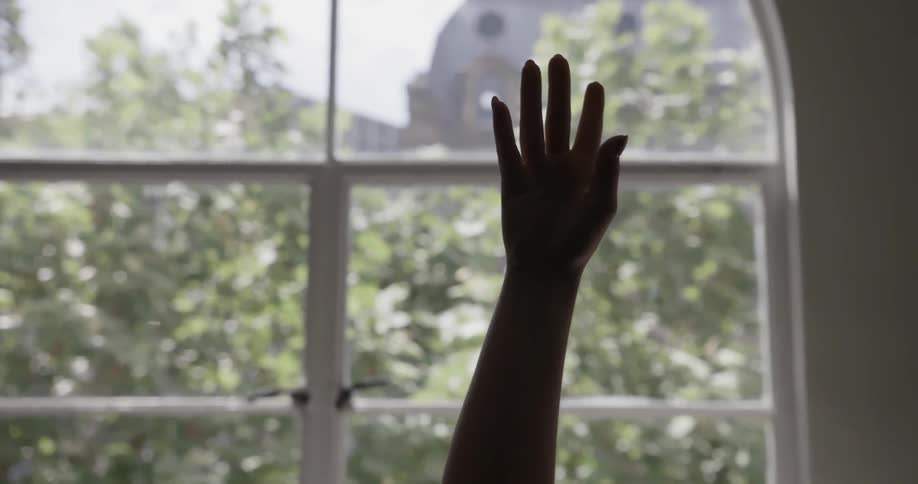 A person raises their hand in front of a window