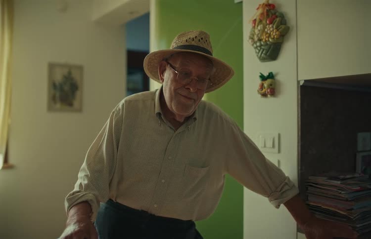 An elderly farmer in a straw hat and glasses smiles warmly during a pleasant conversation in his home