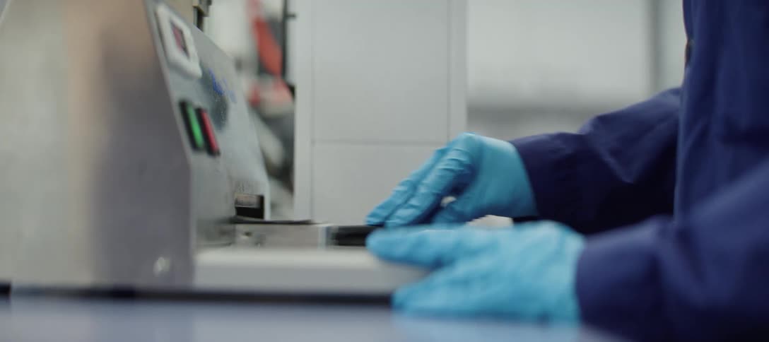 A lab technician wearing protective gloves carefully places a sample into a piece of industrial machinery for testing