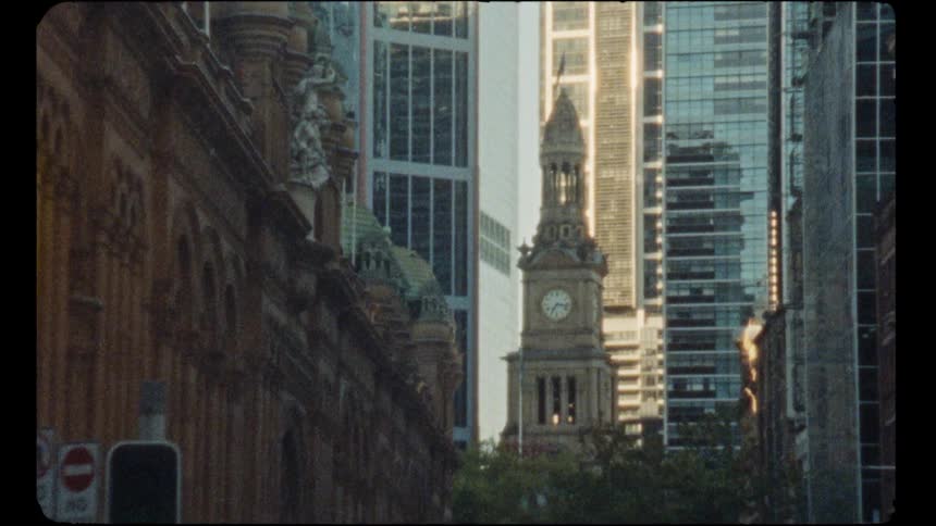 Vintage 8mm film captures a static view of the Sydney Town Hall clock tower nestled between modern downtown skyscrapers
