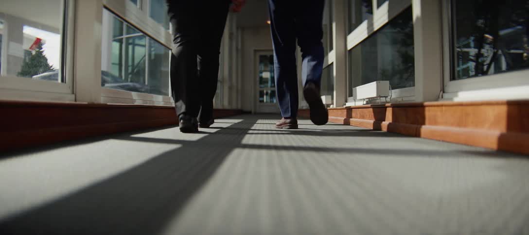 Low angle on the feet of two business professionals walking away down a sunlit office building hallway