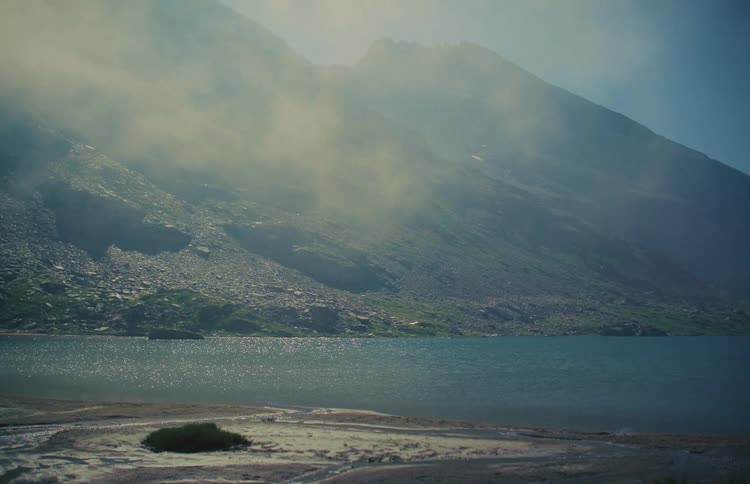 Misty morning sun shines on a serene mountain lake surrounded by rocky slopes