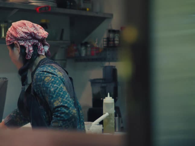 A female chef wearing an apron and bandana prepares food in a professional kitchen