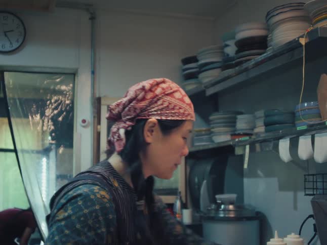 A woman wearing a red bandana diligently works in a dimly lit restaurant kitchen