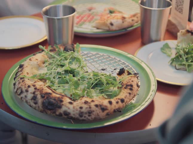 A hand reaches in to grab a delicious slice of Neapolitan pizza topped with fresh arugula at a pizzeria