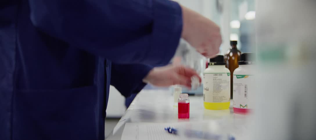 A scientist carefully pours a pink chemical solution into a vial to prepare a sample in a clean laboratory