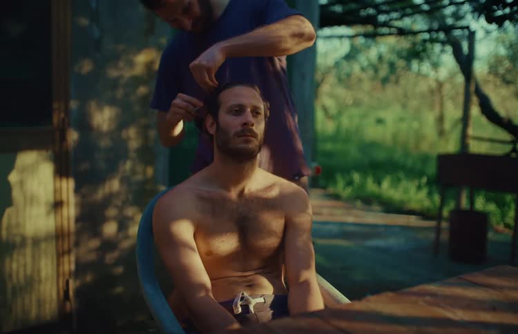 A man gives his friend a haircut with scissors in the backyard during a warm, sunny afternoon