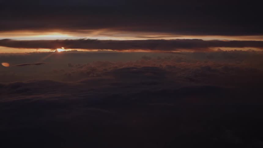 A dramatic sunrise slowly emerges from behind dark clouds as seen from an airplane