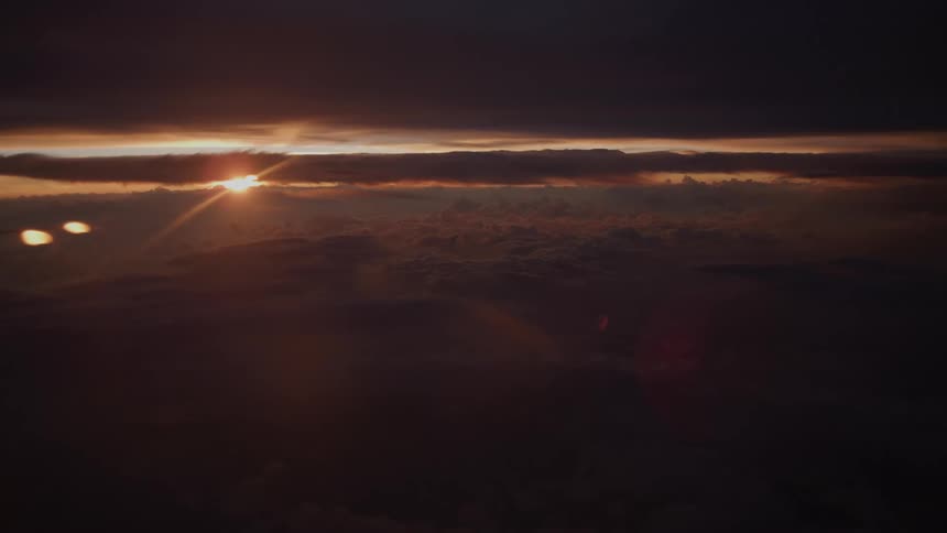 Dramatic aerial view of a dark and moody sunset over a sea of clouds from an airplane window