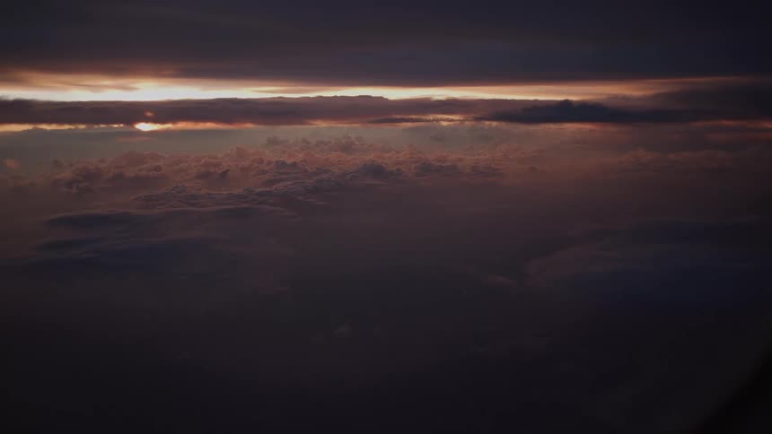 An atmospheric aerial view of dramatic, dark clouds illuminated by a sliver of light from the setting sun