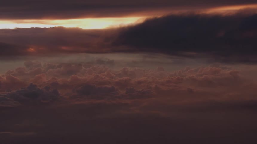 An atmospheric aerial view of a dramatic sea of clouds glowing with warm light at sunset