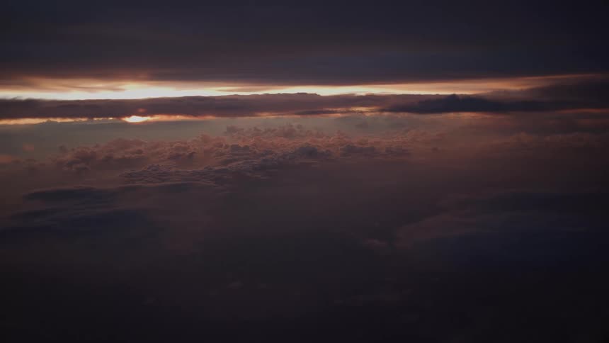 A dramatic aerial view from above a sea of dark clouds as the sun sets on the horizon