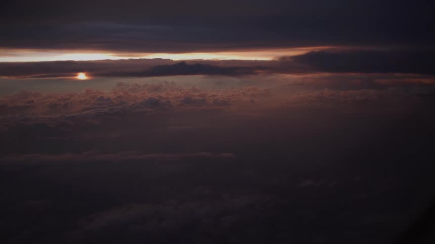 An aerial view from an airplane window captures a dramatic and moody sunset above a vast sea of dark clouds