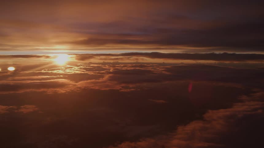 A stunning aerial view captures the sun setting over a vast, dramatic expanse of clouds