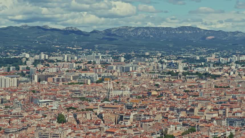 Sweeping panoramic view of the dense cityscape of Marseille, France, with distant mountains under a partly cloudy sky