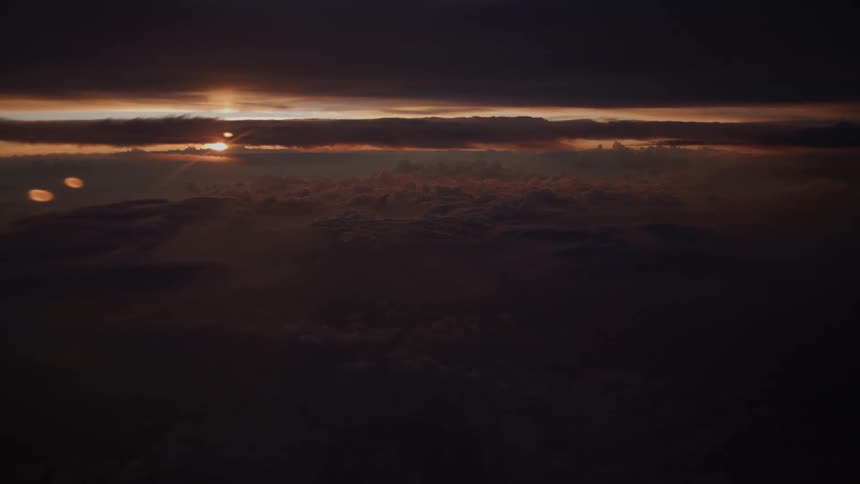 An atmospheric aerial view of the sun setting on the horizon behind a layer of dark, dramatic clouds