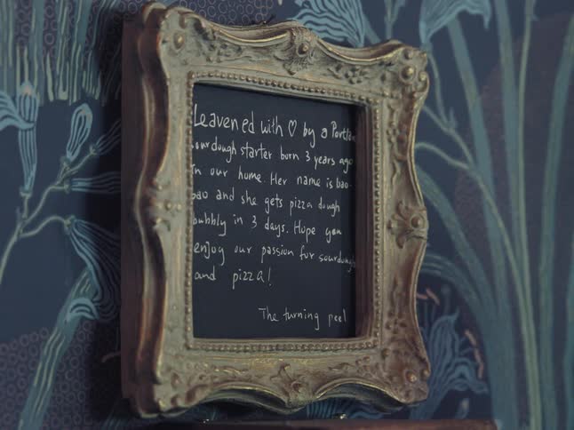 A charming handwritten sign in an ornate frame details the story of a sourdough starter used for pizza at a restaurant