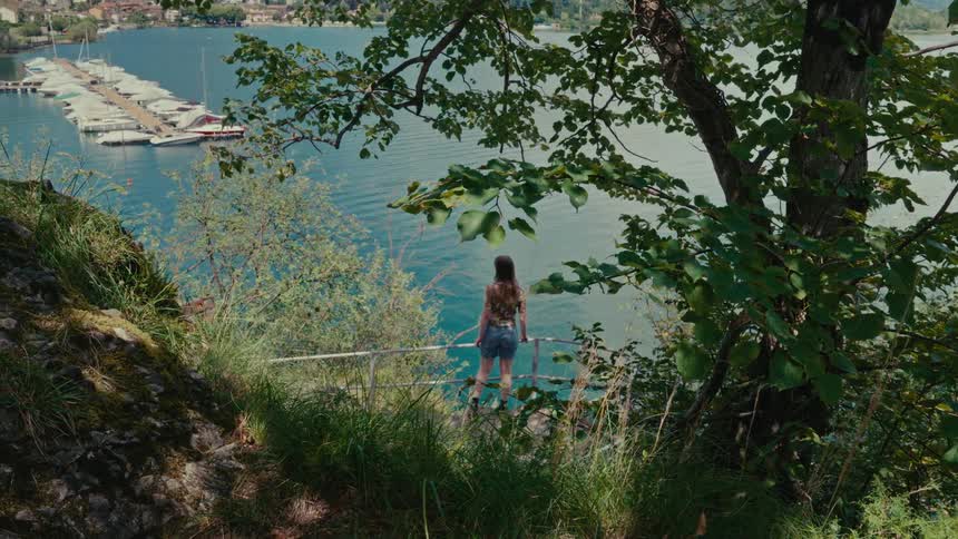 A young woman walks down a nature path to a viewpoint overlooking a beautiful lake and marina on a sunny day