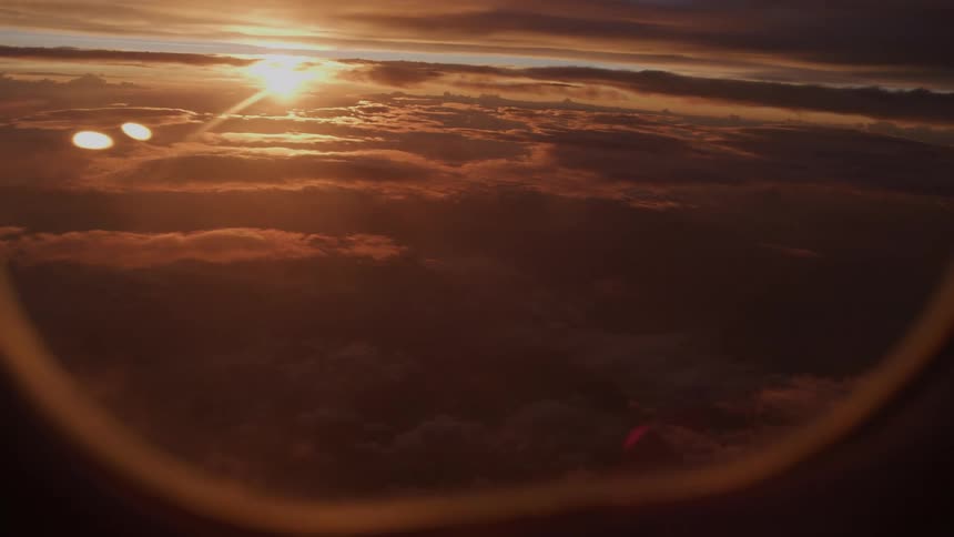 Serene aerial view of a dramatic sunset casting a golden glow over a blanket of clouds, as seen from an airplane window