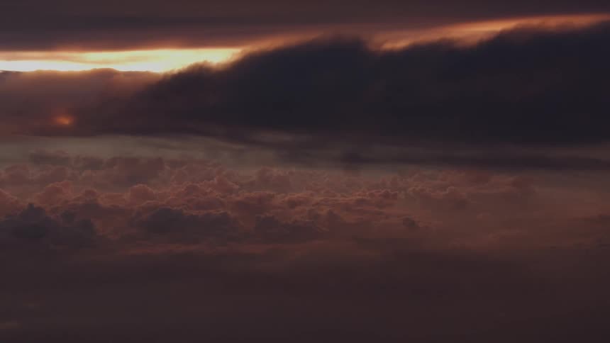 An epic aerial view of a sea of clouds illuminated by the last rays of a setting sun vanishing behind a dark cloud bank
