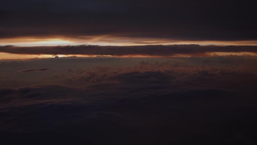 A dramatic aerial view of a dark and moody cloudscape with a sliver of sunset light on the horizon