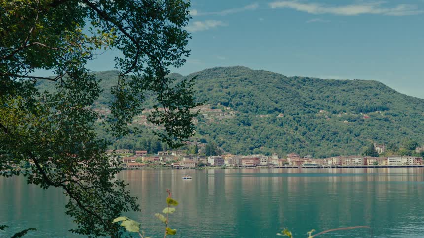 A tranquil lakeside town is nestled at the base of a lush green mountain on a beautiful sunny day