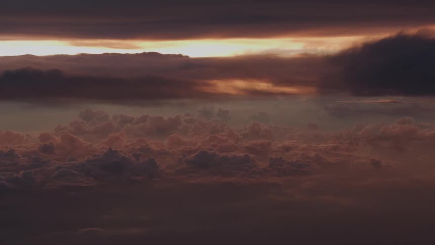 A dramatic and moody sky shows layers of dark clouds illuminated by a golden sunset on the horizon