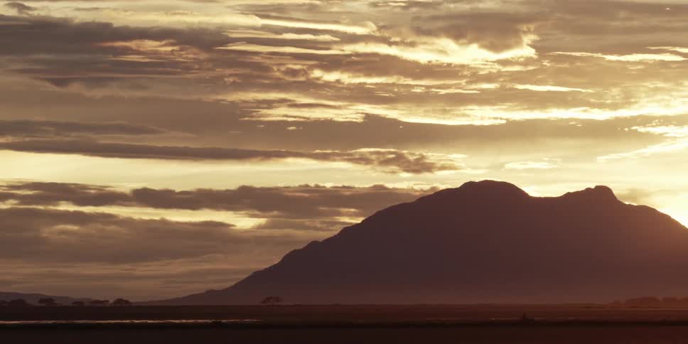 Clouds float over the top of a mountain at sunset