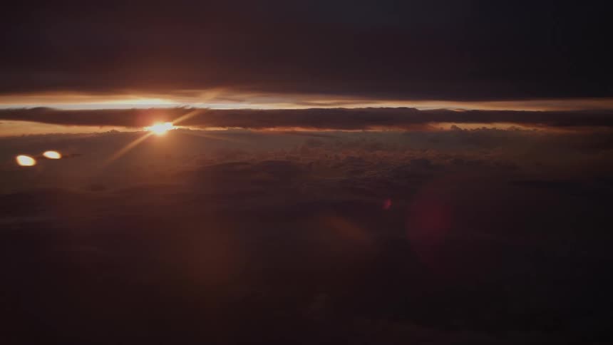A breathtaking aerial view from an airplane window captures the sun setting over a vast sea of dark clouds