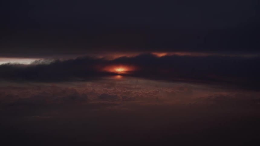 A sliver of the brilliant orange sun peeks through a narrow opening in the dark, heavy clouds during a dramatic sunset