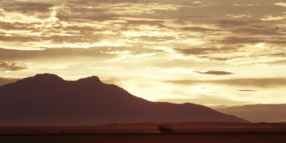 A truck driving while the sun sets behind mountains on a cloudy evening