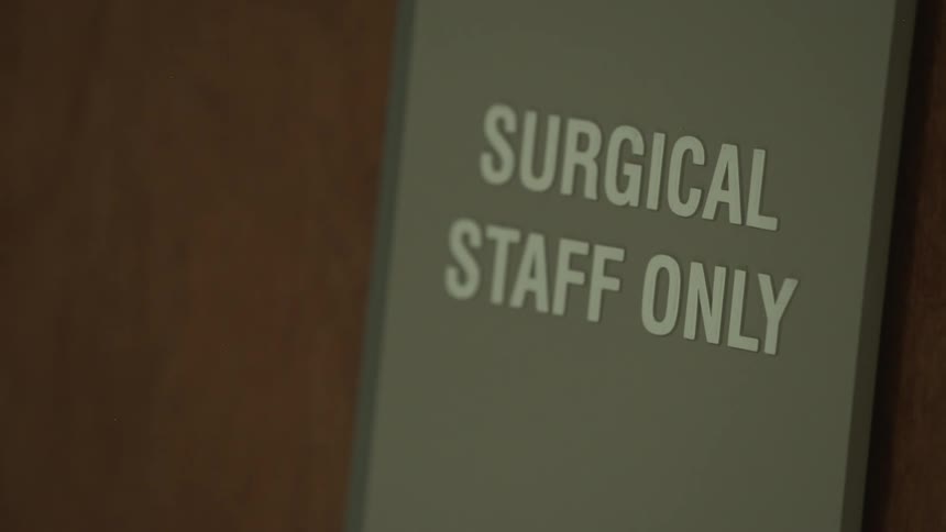 A 'Surgical Staff Only' sign on a door in a hospital goes in and out of focus