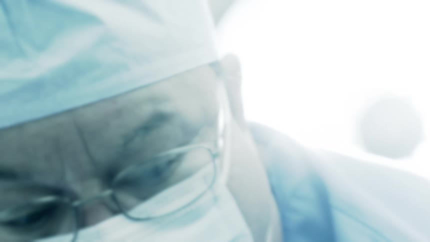 Low angle close-up of a focused surgeon wearing a mask and glasses while operating in a sterile medical environment