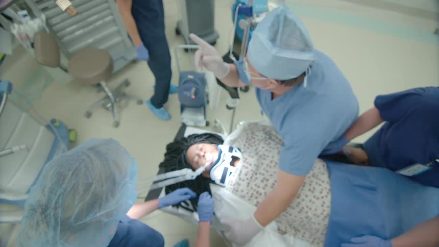 A high-angle, point-of-view shot of a surgical team performing a procedure on a sedated patient in a hospital operating room