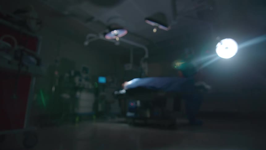 A blurry, low-angle shot of a surgeon working on a patient in a dark and dramatic operating room