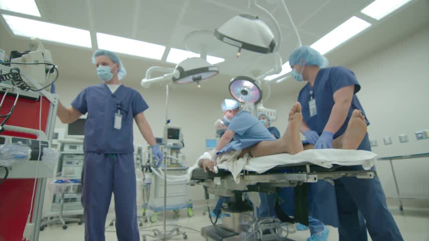 Low angle wide shot of a busy operating room as a team of surgeons and nurses work on a patient