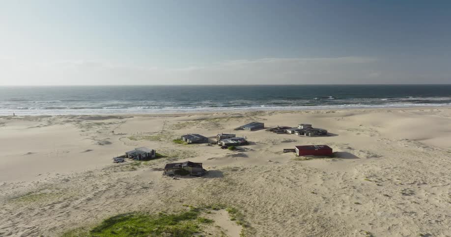 Static aerial view of a remote fishing village nestled in vast sand dunes on a beautiful beach