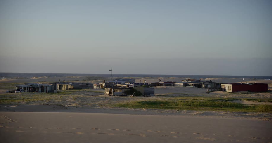 A quiet coastal village with simple homes is nestled among vast sand dunes