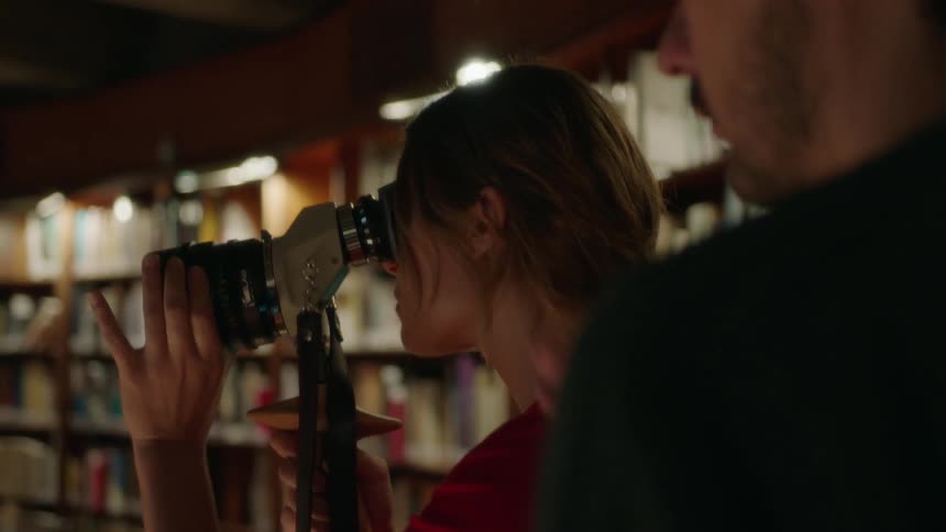 A man talks to a woman who is using a lens in a library