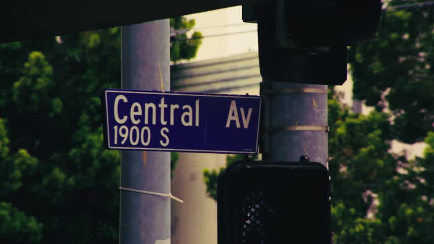 A gritty, close-up shot zooms in on a Central Avenue street sign on a traffic light pole