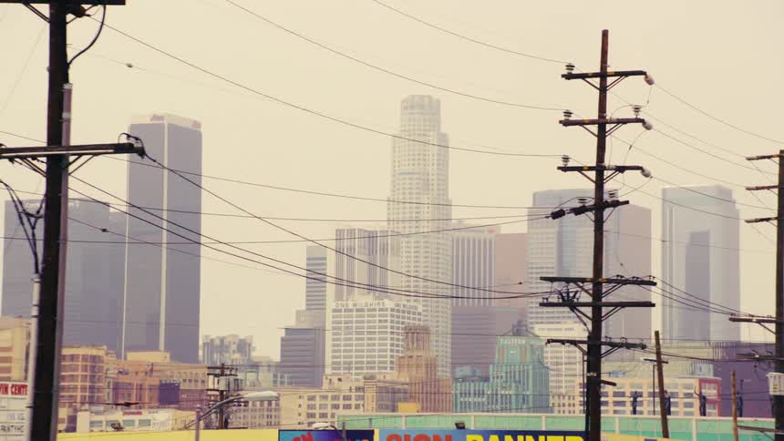 Slow motion view of the Downtown Los Angeles skyline seen from a freeway, framed by power lines and urban infrastructure