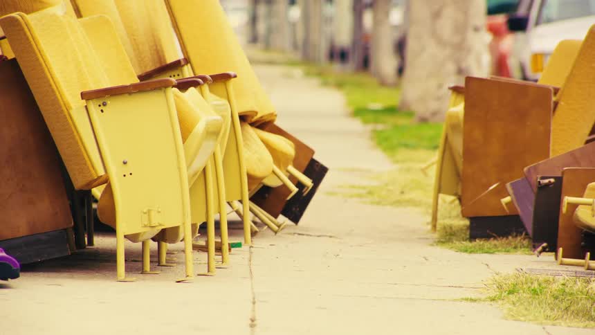Vintage yellow theater chairs are abandoned and piled up on a city sidewalk