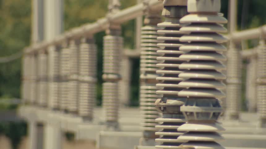 A rack focus shot of high-voltage ceramic insulators at an electrical power substation on a sunny day