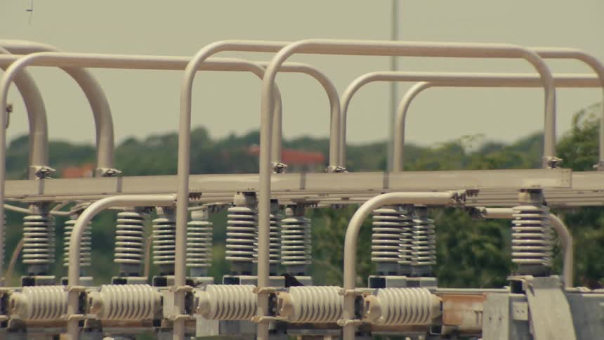 A close-up pan and tilt of a high-voltage electrical substation with insulators and transformers on a sunny day
