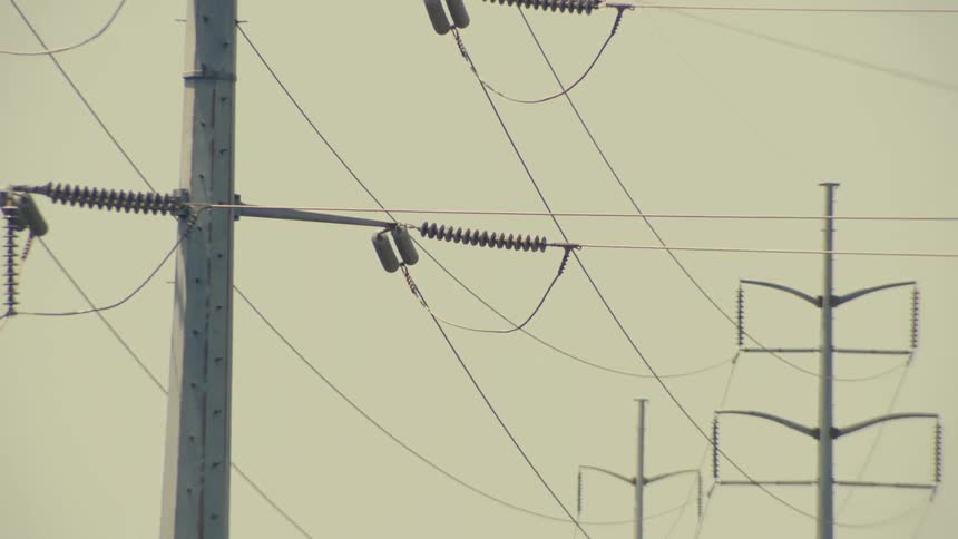 A close-up view of a high-voltage power line pole zooms out to reveal a long row of towers against a hazy sky