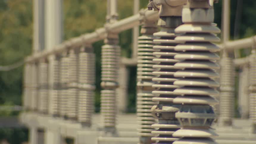 Close-up rack focus reveals rows of ceramic insulators at an electrical power substation